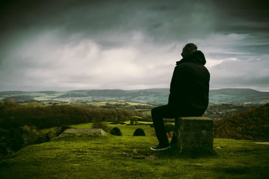 Foto de homem de jaqueta preta sentado vendo a paisagem